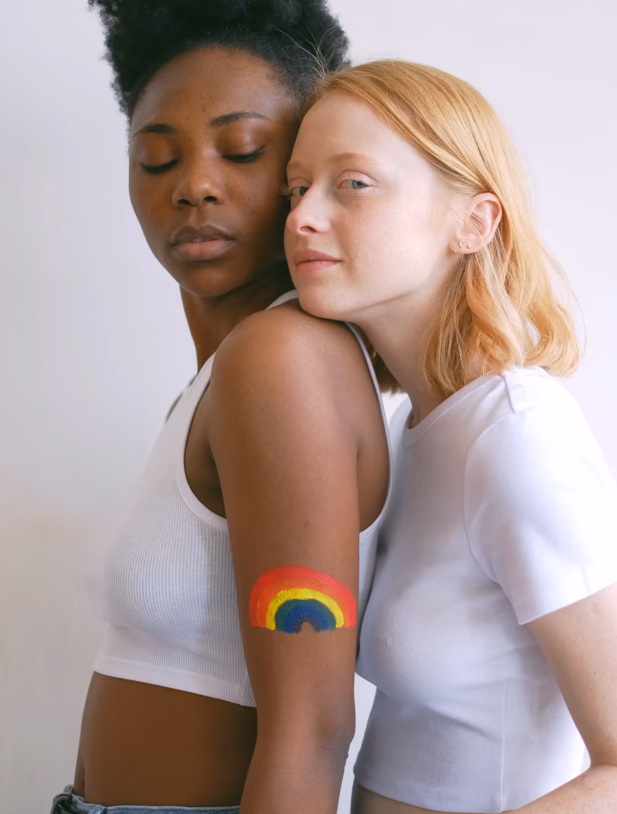 Two women embracing, one with a rainbow painted on her arm